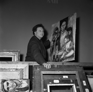 Italian writer and painter Carlo Levi holding one of his paintings, standing behind some picture frames, setting up at the Art Biennale in Venice, 1954 (b/w photo)