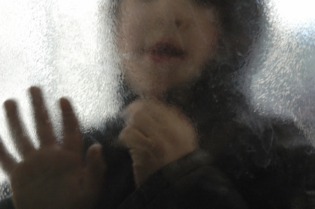 Fuzzy silhouette with hood looking through a glass (departure, farewell, regret).