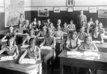 Class of a girls' school with their teacher and a geographic map of Germany hanging at the back of the room. Photography around 1920