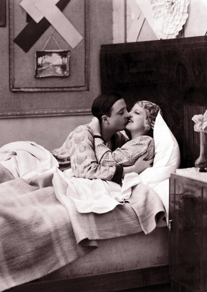 Couple in the bed of a bedroom giving themselves a kiss.