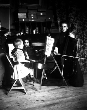 France: staging of a children's orchestra in a bourgeois interior, young girl with cello, little girl with hunting horn, young boy with violin and girl with guitar around a score, 1900
