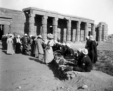 Egypt: Cook cruise, at the gates of a ruined temple, tourists wearing veils buy heads of mummies, 1900