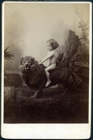 Studio portrait of a child sitting on a dummy lion in an oriental painted decor, 1880