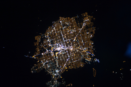 Las Vegas night view - 11/2010 - Las Vegas, Nevada Metropolitan Area at Night - 11/2010 - Las Vegas metropolis night view from the International Space Station (ISS) on November 30, 2010. This image features the Las Vegas, Nevada metropolitan area, located near the southern tip of the state within the Mohave Desert of the southwestern USA. While the city of Las Vegas proper is famous for its casinos and resort hotels, the metropolitan area includes several other incorporated cities and unincorporated (not part of a state - recognized municipality) areas. Astronauts on board the International Space Station observe and photograph numerous metropolitan areas when they are illuminated by sunlight, but the extent and pattern of these areas is perhaps best revealed by the city lights at night. The surrounding dark desert presents a stark contrast to the brightly lit, regular street grid of the developed metropolitan area. The Vegas Strip (image center) is reputed to be the brightest spot on Earth due to the concentration of lights associated with its hotels and casinos. The tarmac of McCarran International Airport to the south is a dark feature by comparison. The airstrips of Nellis Air Force Base on the northeastern fringe of the metropolitan area are likewise dark compared to the well - lit adjacent streets and neighborhoods. The dark mass of Frenchman Mountain borders the metropolitan area to the east. Acquisition of focused night time images such as this one require astronauts to track the target with the handheld camera while the ISS is moving at a speed of more than 7 kilometers per second (15,659 miles per hour) relative to the Earth's surface. This was achieved during ISS Expedition 6 using a homemade tracking device, but subsequent crews have needed to develop manual tracking skills. These skills, together with advances in digital camera technology, have enabled recent ISS crews to acquire striking night time images of the Earth