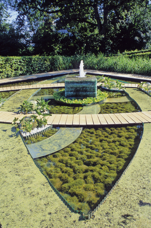 Aquatic Mosaiculture in Chaumont sur Loire, Festival du jardin de Chaumont sur Loire (Chaumont-sur-Loire), 2001. In homage to the beautiful mosaics of Zeugma drowned under the Euphrates, here is an 18th century Anglo-Chinese rococo motif. A crystal gabion fountain dominates the ensemble. The drawing is that of a cross of ellipses made of slatted and water lenses contained in unduline. Clumps of arum serve as a box for plastic flowers hung in aquariums. The goldfish escaped. They swim in the mirrors because the sky has changed into a bathtub to please Greco. A nod to the kitsch, idyllic and well-waxed images of Pierre and Gilles. Reflections in the abime. References for mosaic.