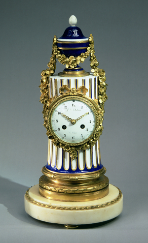 F262 Louis XVI Mantel Clock, of white and blue Sevres porcelain, the dial set in a low column mounted by an urn, with gilt bronze swags, on a marble plinth, dated 1786, movement by Germain Duboss (fl.1757-89)