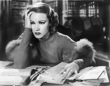Hollywood, California: c. 1923
A young woman holding her head in her hand with a pile of papers on her desk.