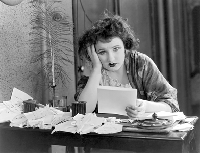 United States: c. 1923.
A woman sitting at a desk with her head in her hand, looking depressed with a pile of papers.