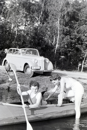 Two young woman are getting inside a boat with a paddle on a lake, Germany 1930s (b/w photo)