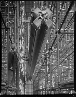 A man standing on scaffolding watching a nave column being hoisted into position during the construction of Coventry Cathedral, 1960 (b/w photo)