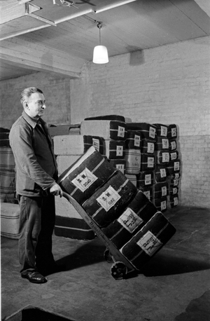 A staff member taking tobbaco bulks at the tobacco silo of the Kyriazi cigarette factory at Hamburg with his barrow, Germany 1930s (b/w photo)