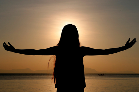 Silhouette of a woman standing by the sea at sunset doing yoga pose and meditation.  Kep.  Cambodia.  (photo)