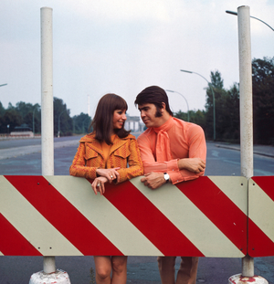 The Israeli musician couple Esther & Abi Ofarim posing in orange clothes in front of the Brandenburg Gate in Berlin; Germany 1967