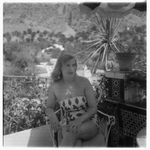 Rose McLaren sitting in a chair outside in a bathing costume, drinking beer in Tangier, early 1960's (b/w photo)
