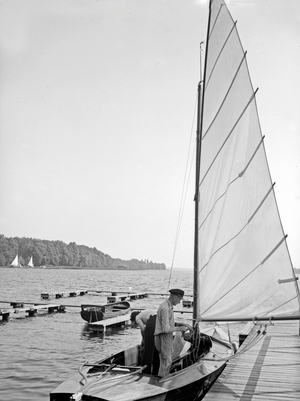 A sailing boat anchoring at a boarwalk at the shore of a lake, Germany 1930s (b/w photo)