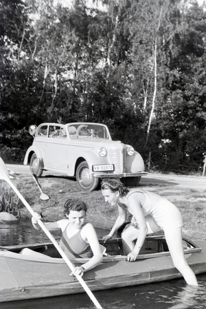 Two young woman are getting inside a boat with a paddle on a lake, Germany 1930s (b/w photo)