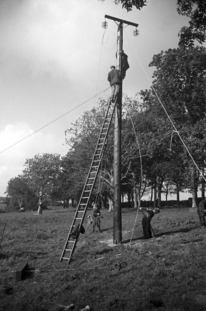 Two men working on the power lines above (b/w photo)