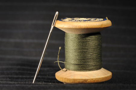 Wooden spool with green thread and darning needle, on black striped cotton (photo)