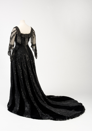Black full length evening gown worn by Queen Alexandra, with bead and sequin decoration and incorporating Queen Alexandra’s signature black silk and gold lettered name tape, made by Barolet of Knightsbridge, London 1908-1910 (silk & velvet)
