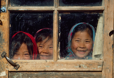 Three children peer out from behind the dirty glass of a wooden door. Damao Qi, In..., 1980s (photo)