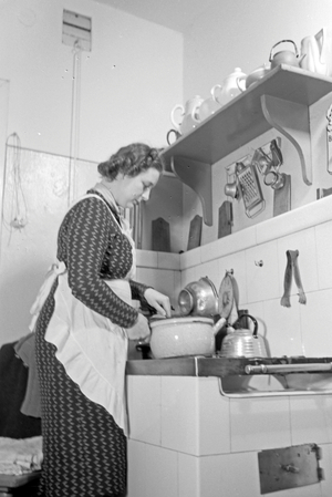 A woman standing in the kitchen on the oven cooking, Germany 1930s (b/w photo)