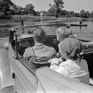 A family crossing a river in their convertible on a ferry boat, Germany 1930s (b/w photo)