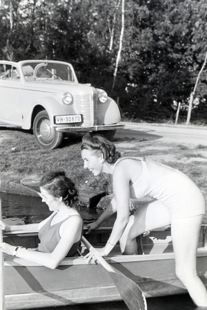 Two young woman are getting inside a boat with a paddle on a lake, Germany 1930s (b/w photo)