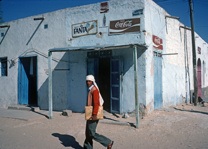 Arab Berger walking in front of building with coca cola and orange drink signs, Tozeur, South Tunisia, Sahara desert, North Africa (photo)