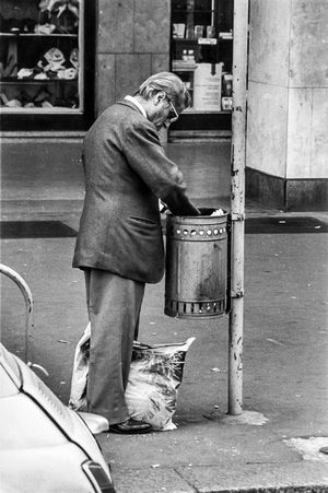 Elderly man looking in a trashcan, near Central Station in Milan, Italy (b/w photo)