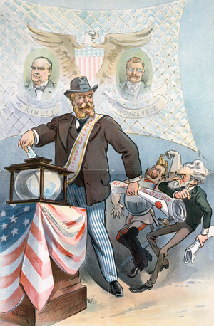 German American man standing in front of a banner showing President William McKinley and Theodore Roosevelt, 1900