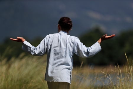 Woman practicing Qi Gong or Tai Chi exercise   in nature.  France.