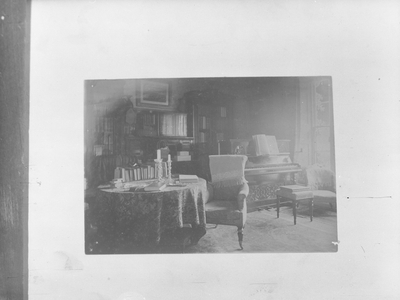 A photograph of a sitting room, including a piano, table, chair, books and candles (possibly at John Ruskin's 'Brantwood'), 1930s-60s (b/w photo)