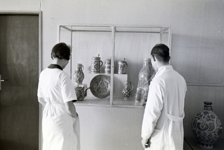 Two students of the College for Ceramics in Höhr-Grenzhausen looking at the ceramics exhibited in the hallway of the school, Germany 1930s (b/w photo)