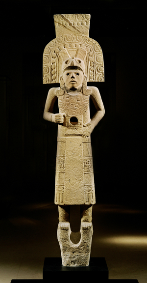 Stone sculpture, male - a warrior or god, carrying a small, skeletal figure like that of a child …