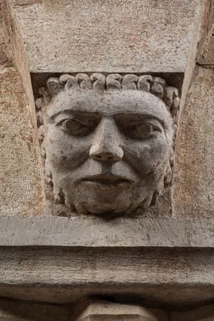 A Corinthian capital with a sculpted face in the abacus protome, by Campionese Masters, XII - XIII century, detail, north wall, Torresani Hall, Ghirlandina Tower, Modena, Italy (photo)