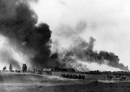 Column of the Wehrmacht passing by a burning village on the Eastern Front, 1941 (b/w photo)