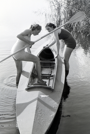 Two young woman are getting inside a boat with a paddle on a lake, Germany 1930s (b/w photo)