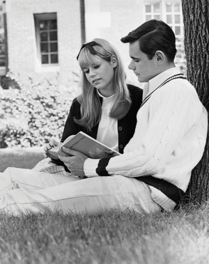 Young couple sitting on grass and reading book