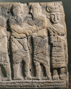 Two warriors embrace before a deity with horned crown and a stern face