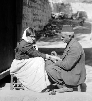 Palestine: Palestinian man tattooing a religious charm on a Christian woman's forearm, c. 1920
