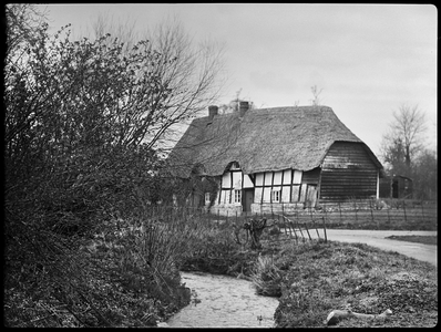 A view of an unidentified timber framed house in Childswickham, showing a thatched roof, eyebrow dormers and a half hipped roof above a weatherboarded end, 1933 (b/w photo)