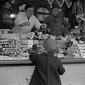 A little boy standing and shopping at the candy booth at the christmas market, Germany 1930s (b/w photo)