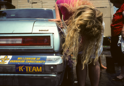 Teenage girl with long blonde hair scrubs a car with a Christian theme bumper sticker…, 1990 (photo)
