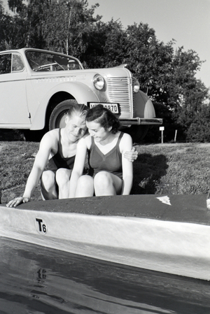 Young couple sitting in front of a boat at the river of a lake, Germany 1930s (b/w photo)