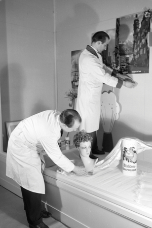 Two window dressers preparing a shop window with products produced and sold by the house of beauty, Germany 1930s (b/w photo)