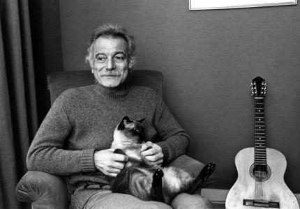 Georges Brassens (1921-1981), French poet, composer and singer, at home with his cat and guitar in 1976 (photo).
