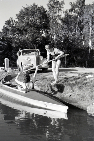 Young couple preparing a boat for paddling at the river of a lake, Germany 1930s (b/w photo)