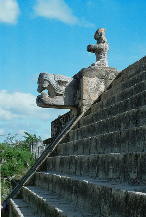 A kneeling figure and the head of a feathered serpent on a landing of the steep stairs which lead to the upper section of the Temple of the Warriors