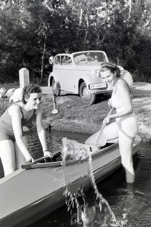 Two young woman are getting inside a boat on a lake with a paddle, Germany 1930s (b/w photo)