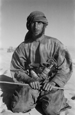 Seated portrait of Wilfred Thesiger, As Saruq, Al Gharbia Region, Abu Dhabi Emirate, United Arab Emirates, March 7-14, 1948 (b/w photo)